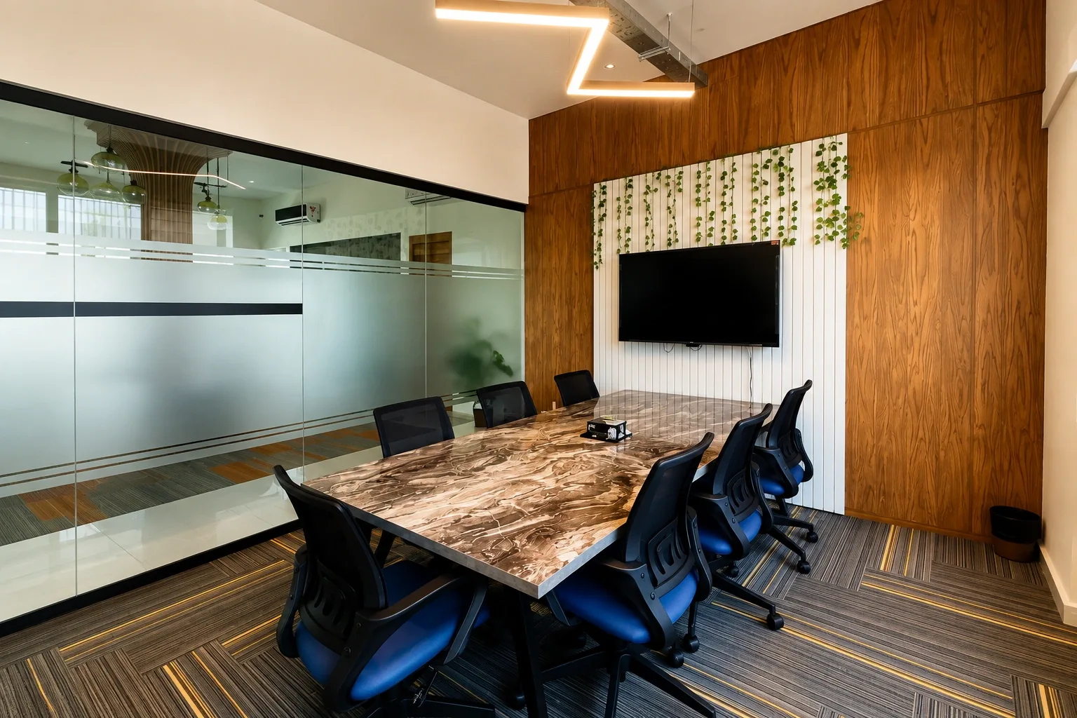 A marble-topped boardroom table with black chairs, a screen and hanging plants