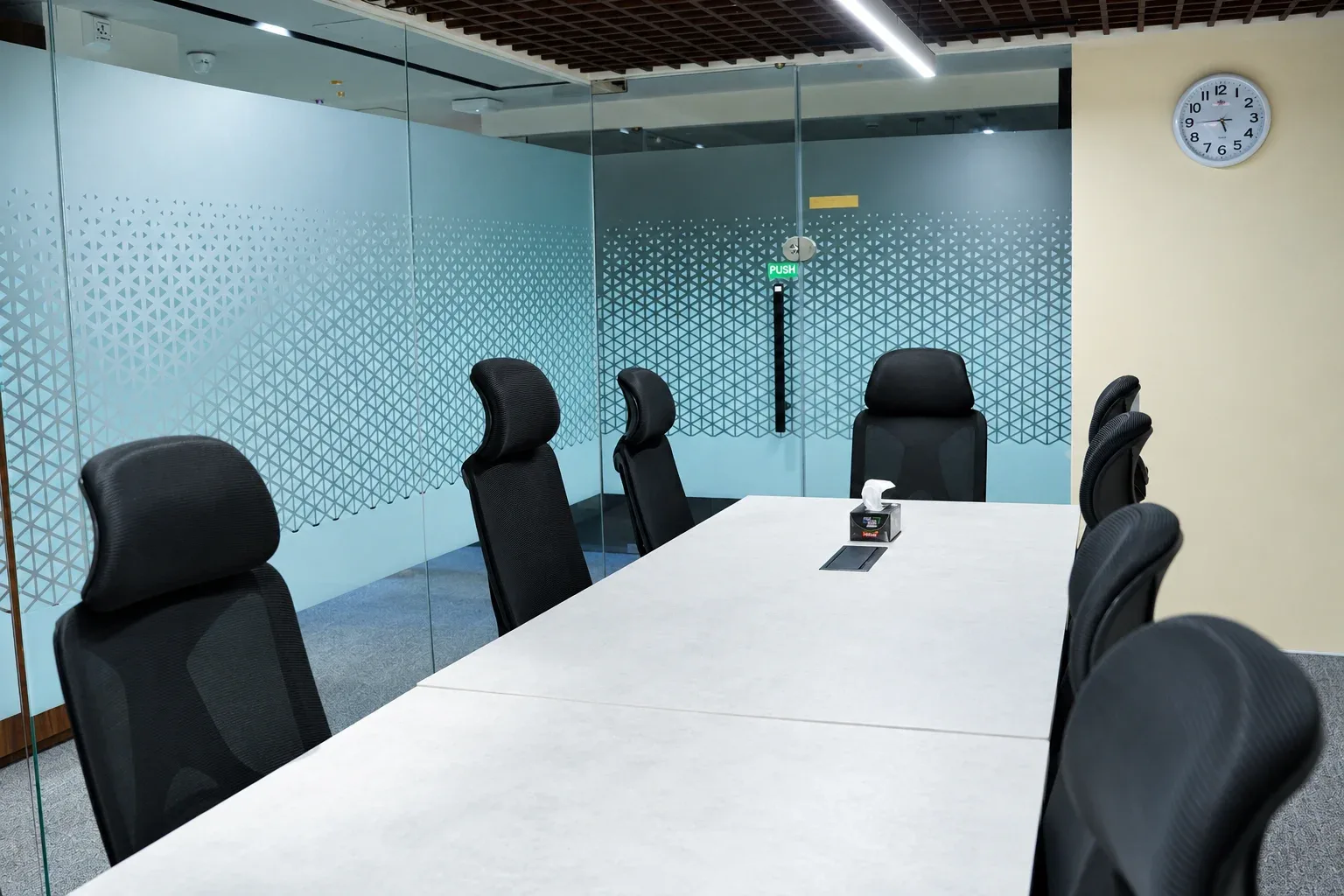 A meeting table with high-back chairs behind patterned frosted glass