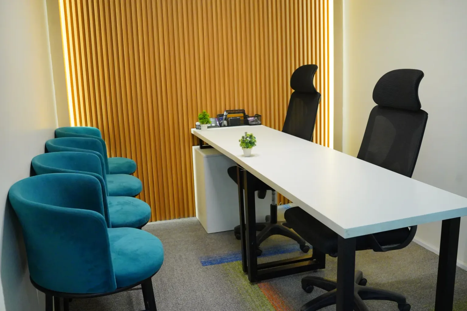 A white table with teal armchairs against a wood-slat wall